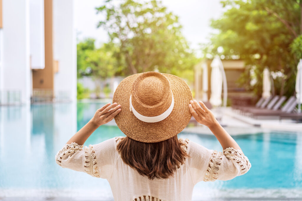young woman traveler enjoying a summer vacation at swimming pool in tropical resort near the beach, travel lifestyle concept